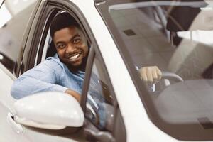 Car Owner. Joyful Afro Guy Smiling To Camera Sitting In New Automobile Driving From Dealership Shop. Selective Focus photo
