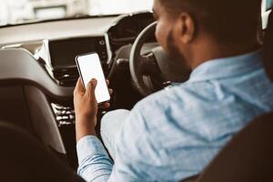 Car Driving App. African American Man Using Phone With Empty Screen Sitting In Auto Vehicle. Selective Focus, Mockup, Back View photo
