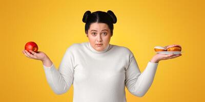 Confused Plus Size Girl Holding Apple And Donuts, Choosing Between Healthy And Unhealthy Junk Food, Yellow Background, Panorama photo