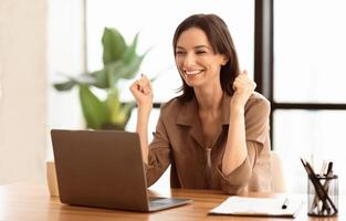 Great Success. Happy manager using laptop, gesturing, celebrating success with clenched fists at office, copyspace photo