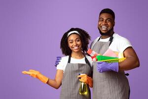 Team of professional cleaners posing with sanitary supplies in hands and pointing aside at copy space over pink background, panorama photo