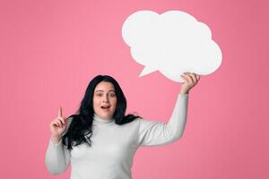 I have idea. Excited overweight woman holding empty speech bubble and pointing finger up over pink background, free space photo
