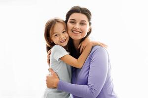 Expecting smiling mom and daughter hugging next to window at home, looking at camera photo