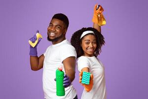 Joyful Spring-Cleaning. Portrait Of Cheerful Black Couple With Sponges And Detergents In Hands Posing On Pink Background In Studio photo