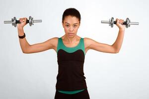 Determined Black Girl Exercising With Dumbbells Looking At Camera Standing Over Yellow Studio Background. Strength Workout Concept. photo