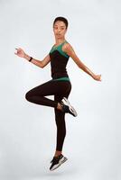 Fitness. Black Woman Jumping Exercising In Studio Over Yellow Background. Vertical, Full Length photo