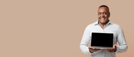 Useful website. Middle aged afro man showing laptop with blank screen, orange studio background photo