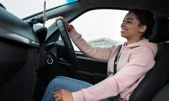 Great friendly taxi driver, auto blogger and car traveler. Smiling millennial african american woman holding steering wheel, changing speed, looking at road, driving car in rain, profile, empty space photo
