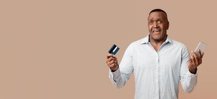 Online transaction problem. Confused middle african american man using mobile banking and credit card photo