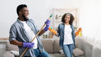 Tidying With Fun. Joyful Black Couple Fooling While Cleaning Flat Together, Man Using Mop Handle As Guitar And Laughing photo