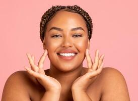 Facial Skincare. Attractive Black Woman Touching Face Moisturizing Smooth Skin Posing Smiling To Camera Over Pink Background In Studio. Beauty Routine And Pampering Concept photo