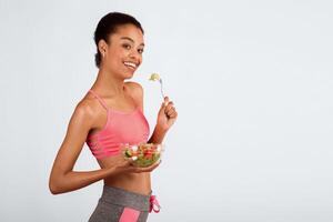 Workout And Nutrition. Black Girl Eating Vegetable Salad From Bowl Standing On Pink Studio Background. Copy Space photo