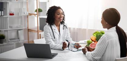 Cheerful dietologist showing female patient how to use mobile app for counting calories, clinic interior, free space photo