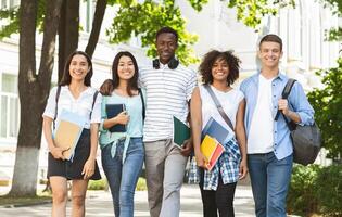 Cheerful college students walking out of campus together, and posing at camera outdoors, having break in classes, free space photo