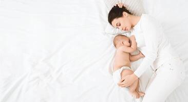 Sweetest dream with baby. Mother embracing her napping baby in bed, sleeping together, top view with empty space photo