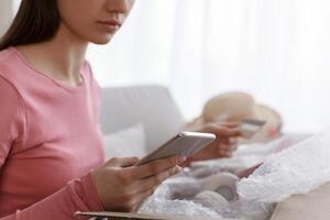 Woman unpacking online order and using cellphone for checking delivery package or return it to the shop photo
