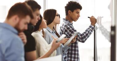 Student boy writing answers to tasks on whiteboard in class, classmates taking notes photo