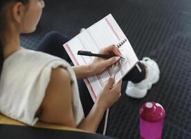 Workout planning. Young woman making her workout schedule in notebook indoors, above view photo