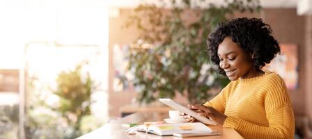 Smiling african girl beauty blogger working with digital tablet online at cafe, empty space photo