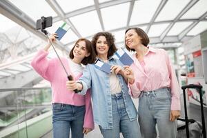 Three friends enjoy a lighthearted moment at the airport, capturing a selfie while holding their boarding passes. They are excited for their upcoming journey together. photo