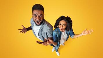 Top View Of Angry Black Couple Emotionally Reacting To Something, Objecting With Raised Hands, Standing Together On Yellow Studio Background photo