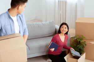 College Materials. Charming asian girl giving book to her friend while packing for moving in or out of the dorm photo