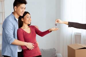 Own House Concept. Unrecognizable female agent giving keys to smiling asian couple, empty space photo