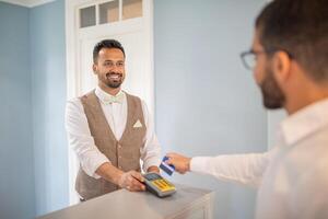 A welcoming hotel receptionist helps a guest process a payment at a modern front desk. The atmosphere is bright and inviting, showcasing attentive customer service. photo
