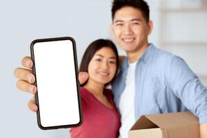 Homeowners. Smiling chinese couple showing key to camera, man holding box, selective focus, copy space photo