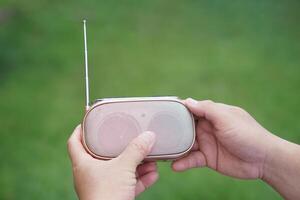 Hands hold portable mini radio. Concept, audio electronics for listening to music, songs or news from radio wave channel station. Analog amplifier for relaxation and lifestyle. photo