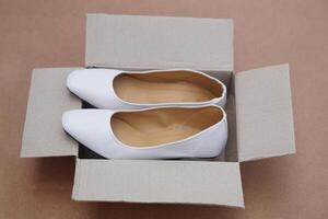 White shoes in brown cardboard box from shopping online or shoe shops. Concept, fashion, formal and polite footwears to match with white uniform or outfit. New shoes. photo