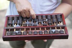 Close up man hand calculate and count wooden abacus. Concept, ancient style calculation. Counting equipment. Calculator. Educational material. Math teaching aid photo