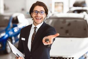 Car Rent. Handsome Agent Showing Auto Key Standing In Automobile Rental Office. Copyspace, Shallow Depth photo