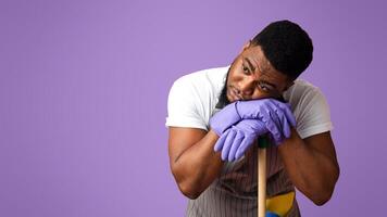 Exhausted Black Guy Leaning On Mop Handle, Resting Head On Hands Tired After Cleaning, Standing Over Pink StudioBackground With Free Space Done photo