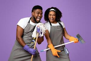 Cleaning Fun. Playful Black Couple Using Mop As Microphones, Having Fun During Tidying, Singing Together Over Pink Background, Copy Space photo