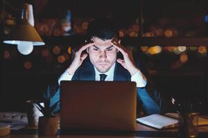 Concentrated Businessman At Laptop Thinking On Business Project Working Overnight In Modern Office. photo