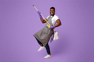 Funny African Man Using Mop Handle As Guitar, Having Fun During Cleaning. Posing Over Pink Background In Studio, Copy Space photo