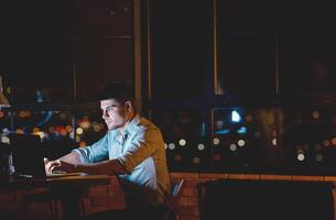 Businessman At Laptop Working Overnight Sitting In Modern Office Near Window With Panoramic View. Empty Space photo