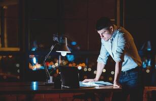 Business Man Working On Laptop Standing In Modern Office Late At Night. Empty Space For Text photo