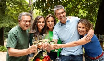 A group of five friends joyfully raises their glasses of sparkling wine in a beautiful park. They smile warmly, enjoying each other's company on a sunny, summer day surrounded by nature. photo