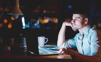 Overnight Work. Tired Businessman At Laptop Sitting Touching Chin Working In Modern Office Late At Night. Low Light photo
