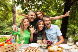 A group of five friends joyfully poses for a picture during a lively outdoor picnic, surrounded by delicious food, drinks, and greenery in the afternoon sunlight. photo