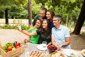 A group of five friends gathers around a table loaded with fresh fruits and snacks, smiling as they take a selfie in a vibrant garden during a summer day. photo