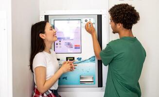 A young man helps a woman use a vending machine that dispenses various products, showcasing a friendly interaction in a relaxed environment. photo