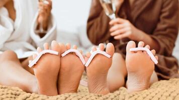 Close up of women feet with toe separators on, multiracial girlfriends having spa day at home, drinking champagne, panorama, pedicure concept photo