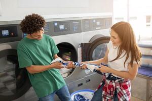 Two young adults are happily folding laundry together at a laundromat, enjoying their time as they chat and share a moment on a sunny afternoon. photo