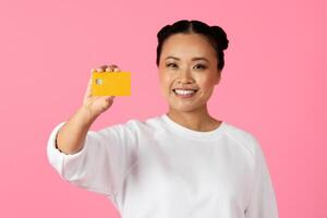 A cheerful Asian woman displays a yellow card while standing in front of a bright pink backdrop. Her joyful expression suggests enthusiasm and positivity. photo