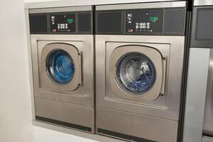 Two stainless steel washing machines in a bright, modern laundromat display their tumbling laundry. The area is well-lit, creating a welcoming atmosphere for customers. photo