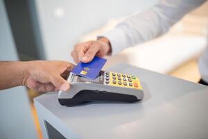 A customer is making a contactless payment by tapping a card on a payment terminal at a retail checkout. The cashier assists with the transaction in a bright store environment. photo