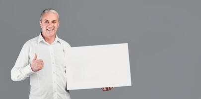 I Recommend. Smiling Senior Man Holding Blank Placard With Copy Space, Showing Thumbs Up, Gray Studio Wall photo